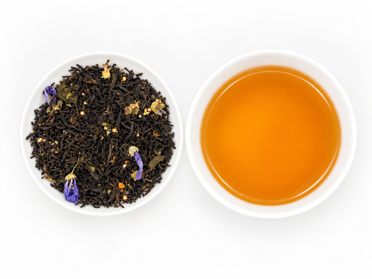 Earl Grey Blueberry – aromatisierter Schwarztee mit dunklen Teeblättern und einzelnen violetten Blüten, daneben eine weiße Schale mit klarem, goldorangefarbenem Teeaufguss.