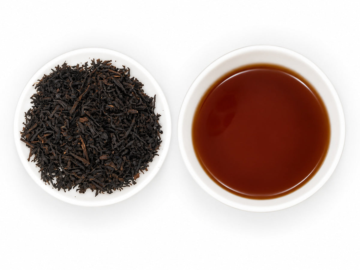 Earl Grey Klassic – aromatisierter Schwarztee mit dunklen, länglichen Teeblättern auf einem weißen Tellerchen, daneben eine weiße Teeschale mit klarem, dunkelbraunem Teeaufguss.
 Kopieren