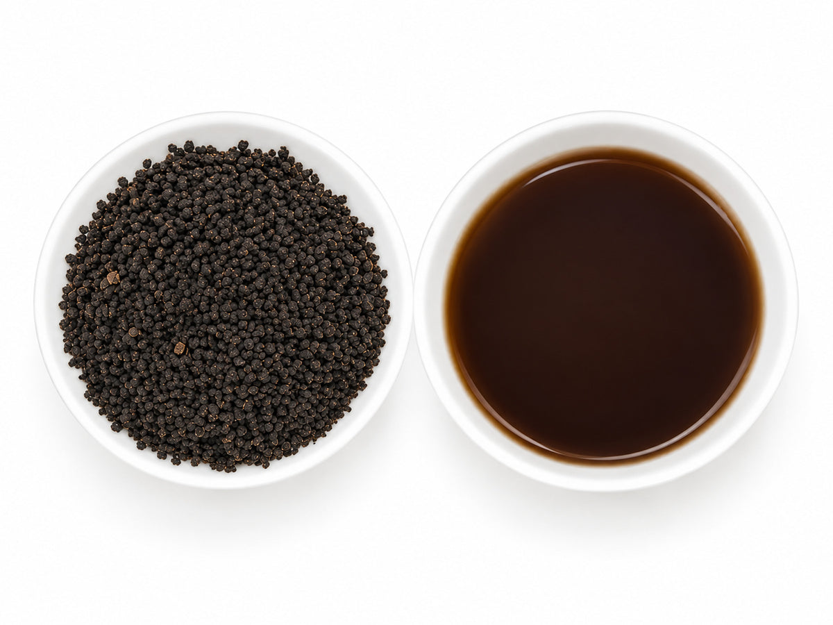 Irish Breakfast Broken CTC Assam Blend Schwarztee mit kleinen, dunkelbraunen Teeblattkügelchen in einer weißen Schale, daneben eine Teeschale mit kräftigem, dunkelbraunem Aufguss.